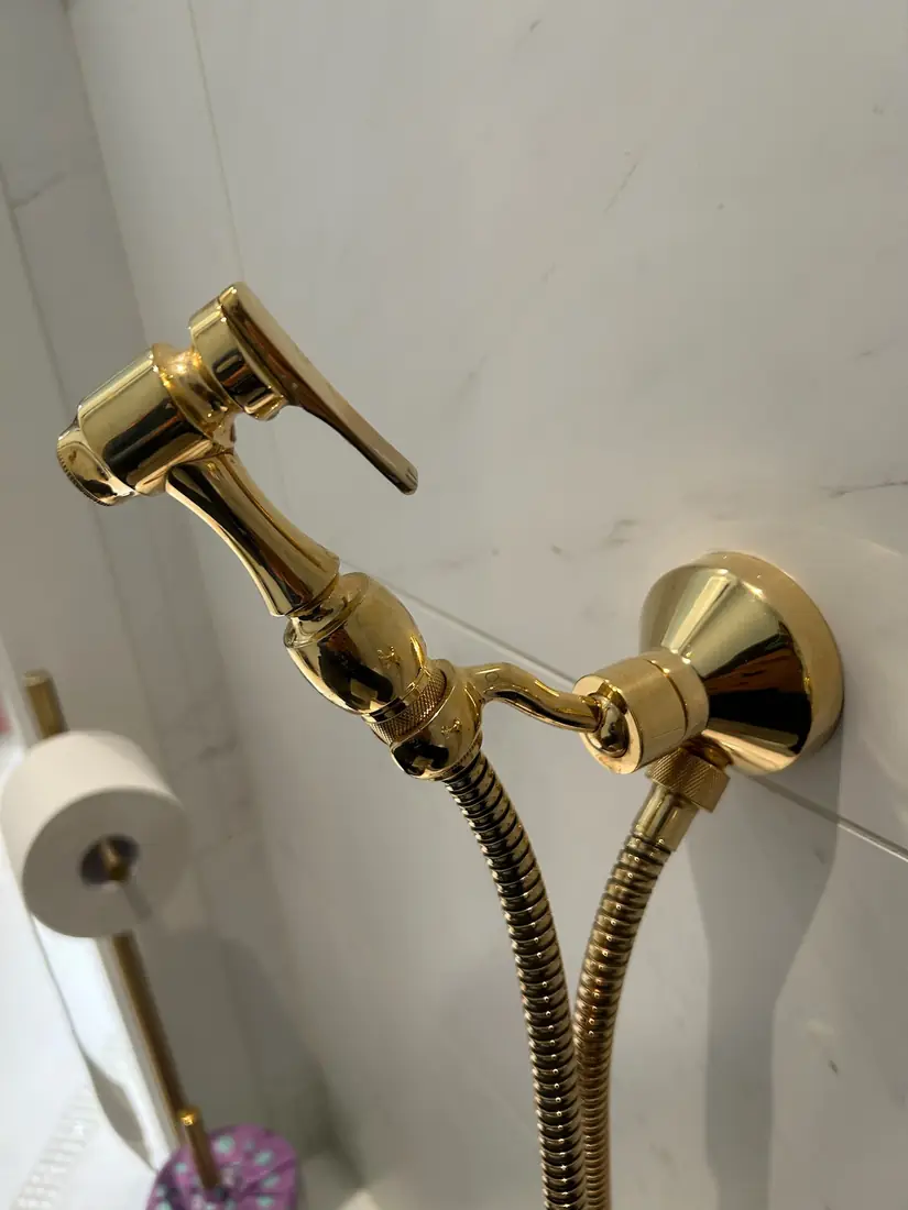 Polished brass bidet sprayer mounted on a marble wall