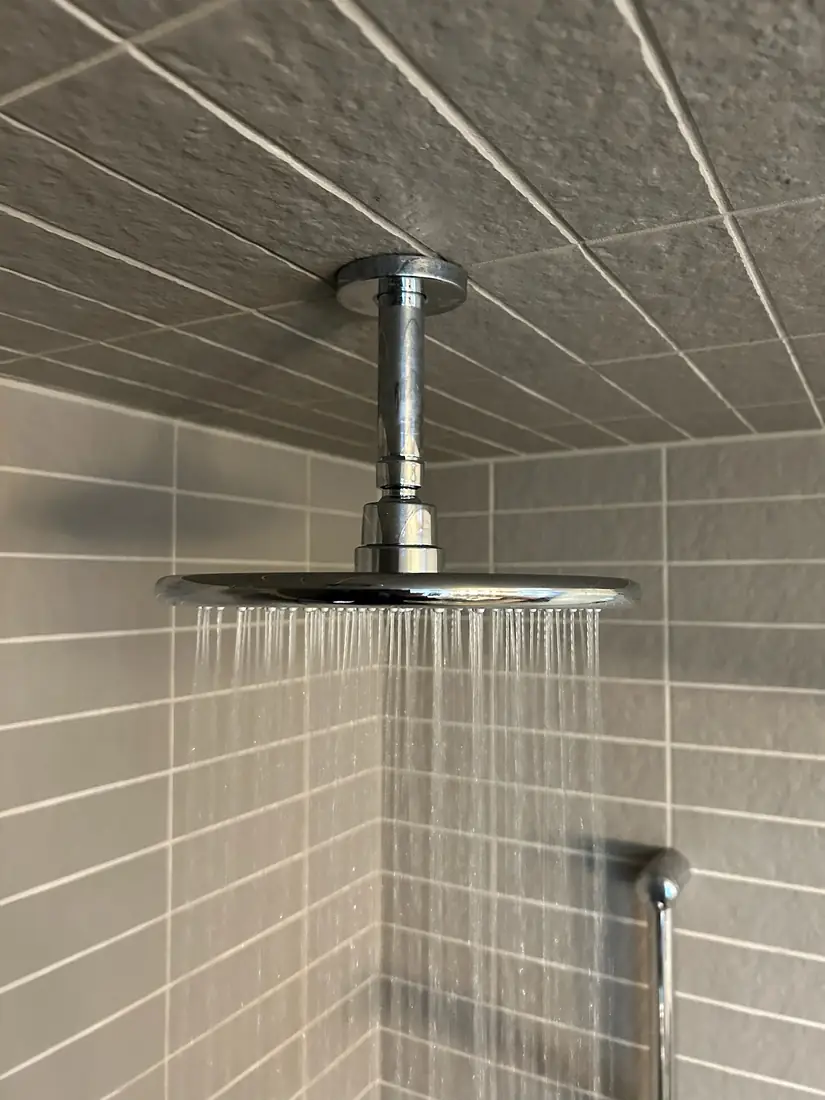 Ceiling-mounted rain shower head running in a finished tiled shower